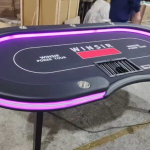 An oval - shaped poker table with purple LED lighting, branded "WINSIR POKER TOUR", situated in an industrial or workshop setting.