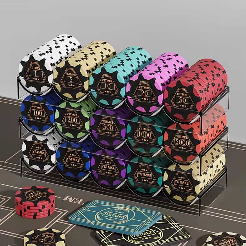A transparent acrylic rack holding various stacks of colorful poker chips with denominations labeled "YSTMIKE", placed on a poker - themed surface along with some playing cards.