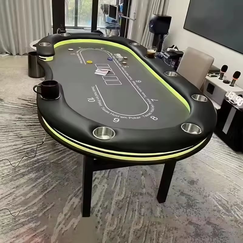 An oval - shaped Texas Hold'em poker table with green LED lighting, black surface, and various poker - related markings, set in a well - furnished room with a carpeted floor.