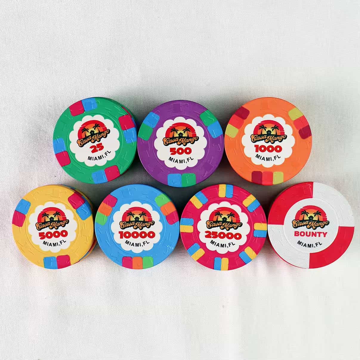 A set of colorful poker chips labeled "Easy Hang, Miami, FL" with various denominations, including 25, 500, 1000, 5000, 10000, 25000, and "BOUNTY", arranged on a white surface.